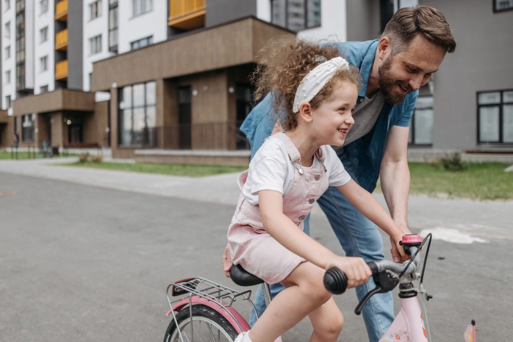 enfant apprenant à faire du vélo avec son père qui la pousse